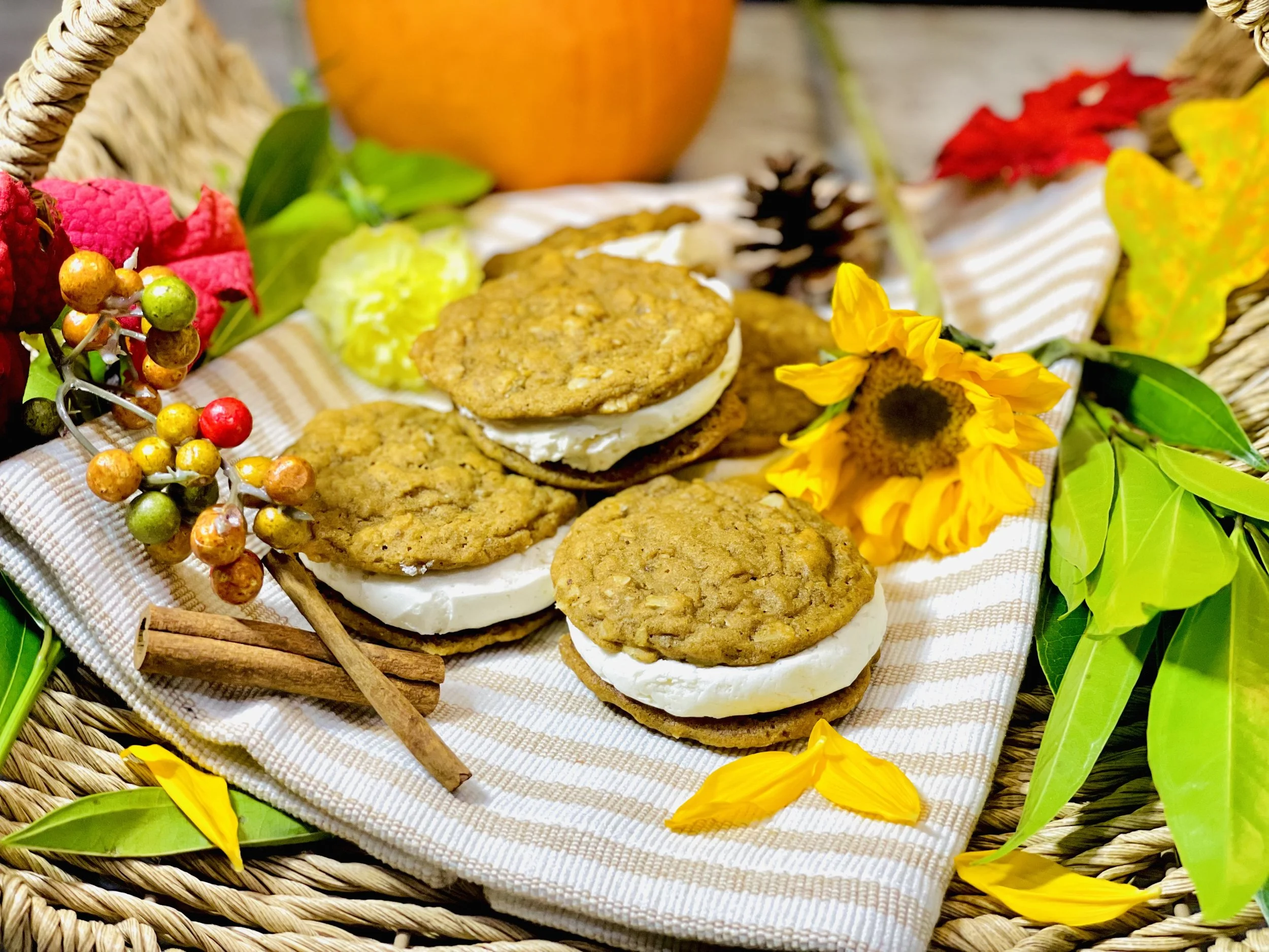 Vegan Pumpkin Spice Oatmeal Cream Pies displayed in a fall-themed basket with flowers and cinnamon sticks.