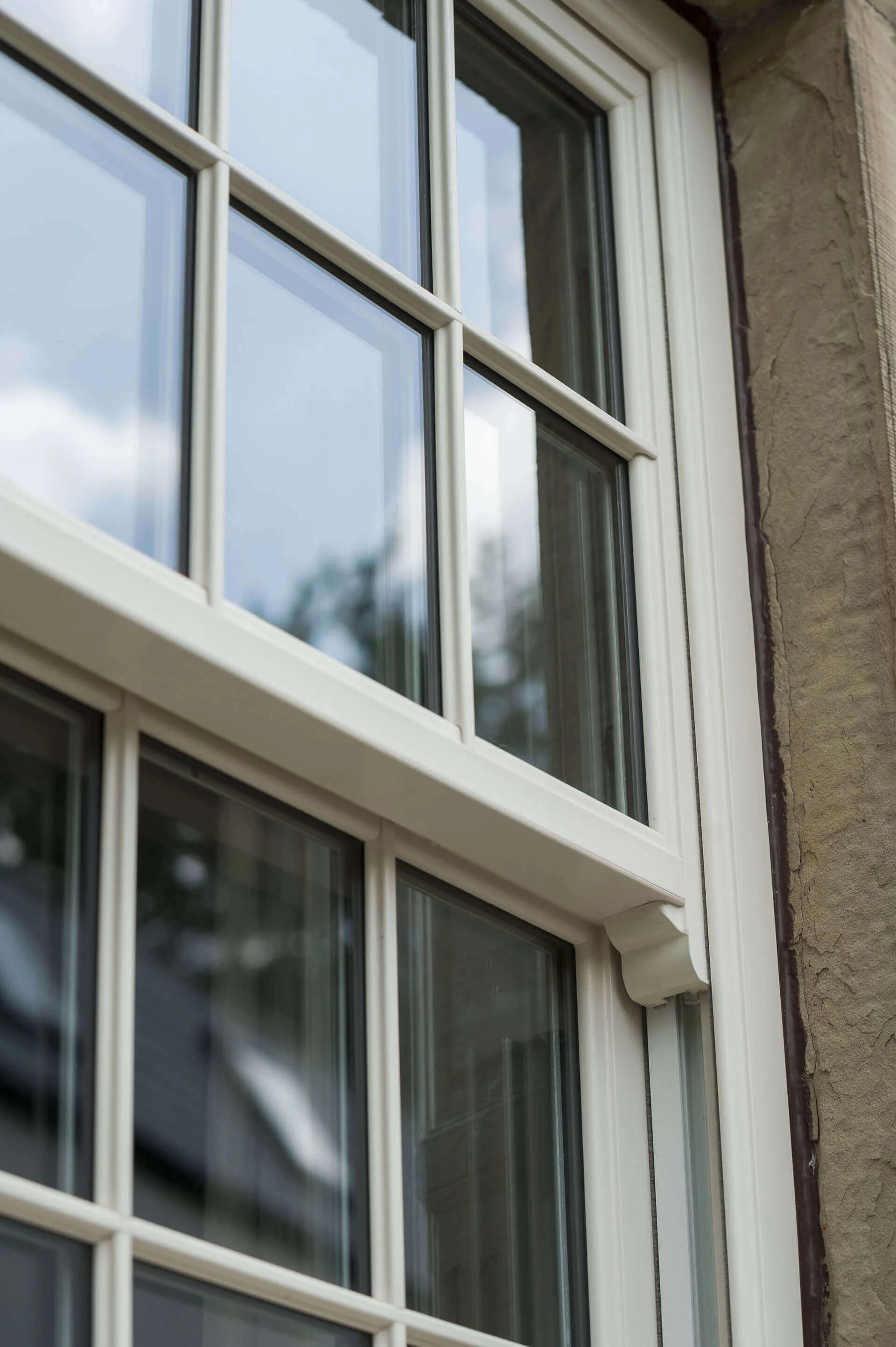 Close-up of a multi-pane window on a brick wall, with reflections of the sky and trees in the glass.