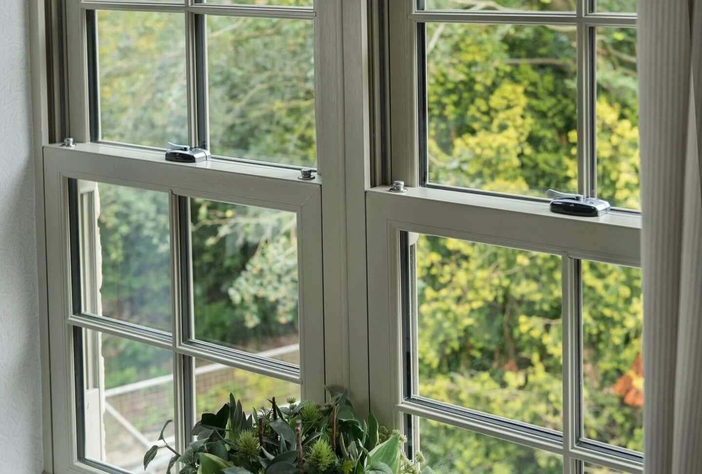 Close-up view of a white multi-pane window with window locks, overlooking green trees and foliage outside.