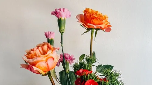 A colorful floral arrangement featuring orange and pink carnations, photographed against a plain white background — a sample reference image from a free inspiration binder offering creative resources for artists.