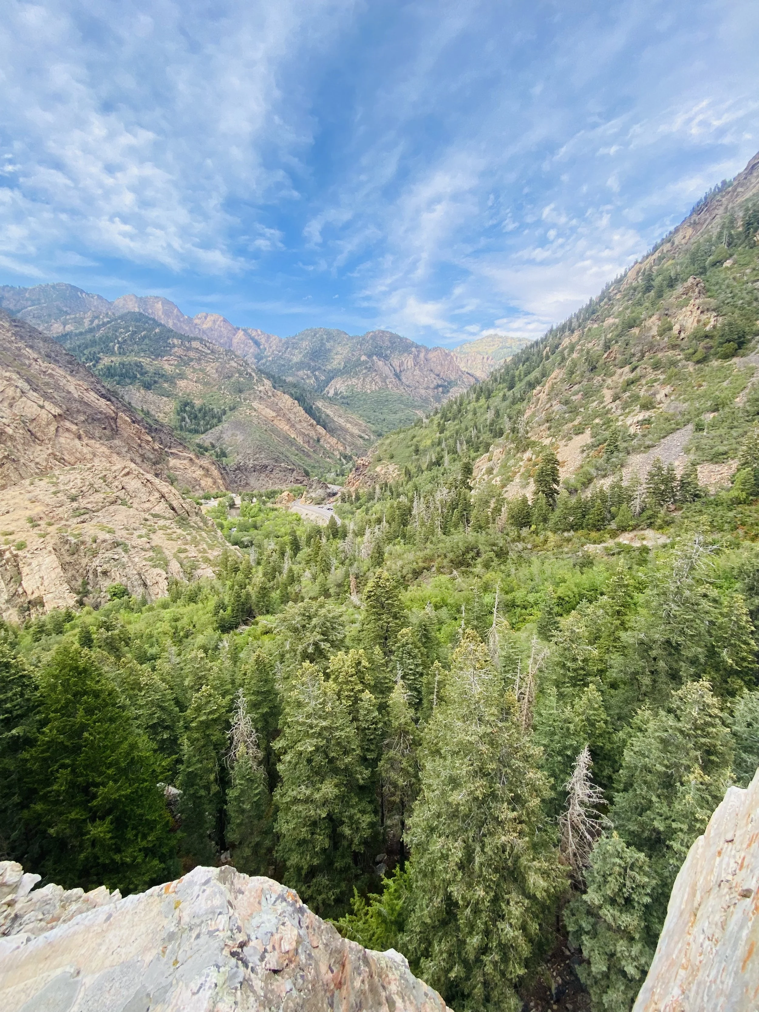 A scenic view of a green forested valley surrounded by mountains under a blue sky with scattered clouds.