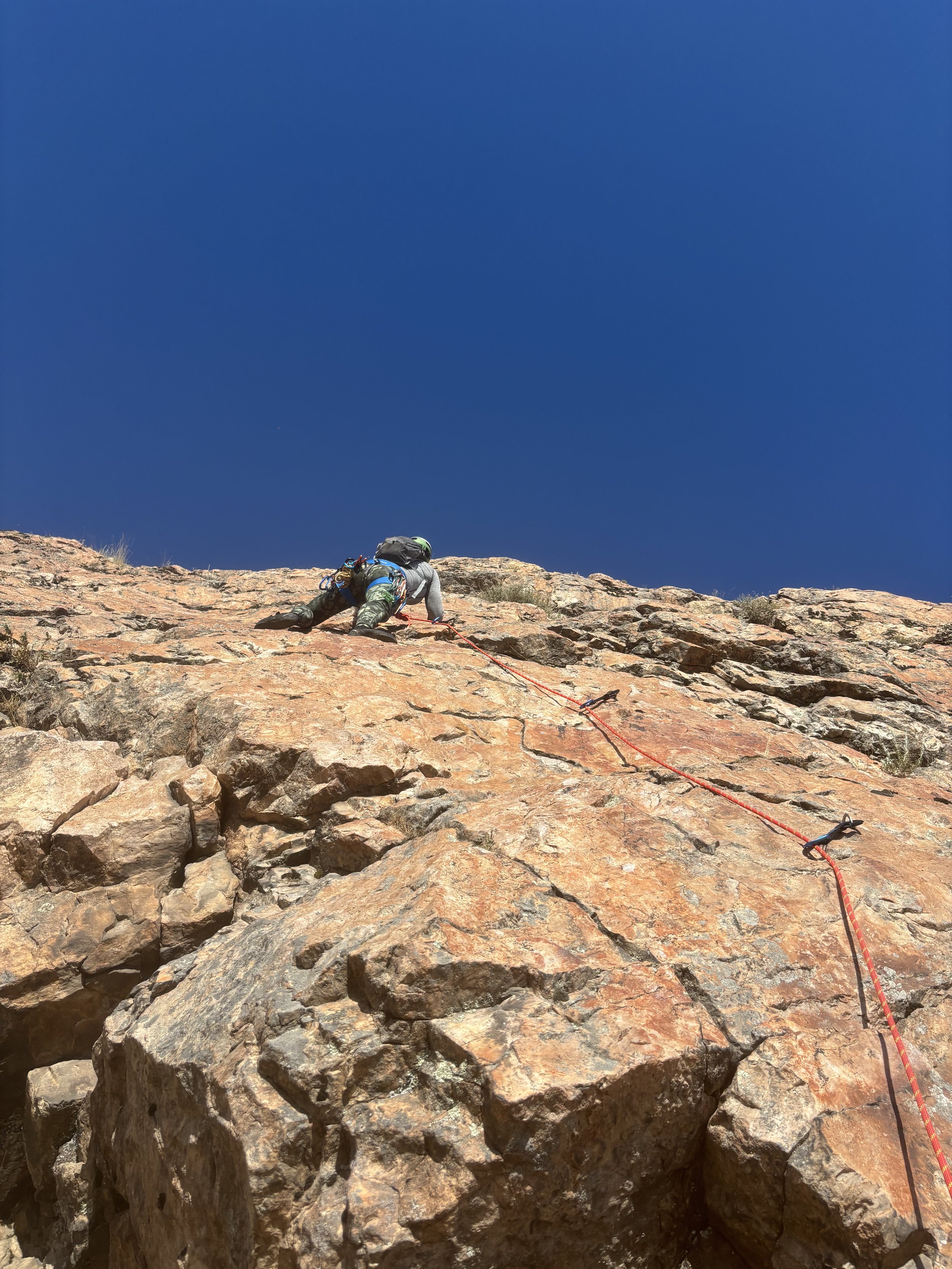 A person climbing a steep rocky mountain with a safety rope under a clear blue sky.