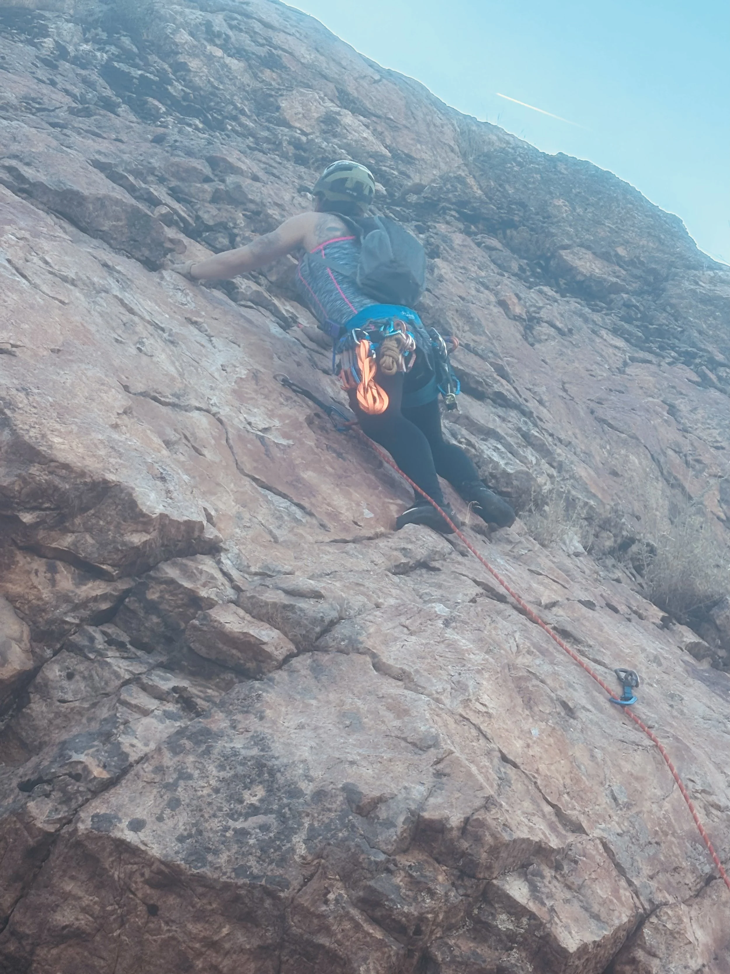 A person wearing a helmet and climbing gear ascending a rocky cliff face, with a safety rope attached.