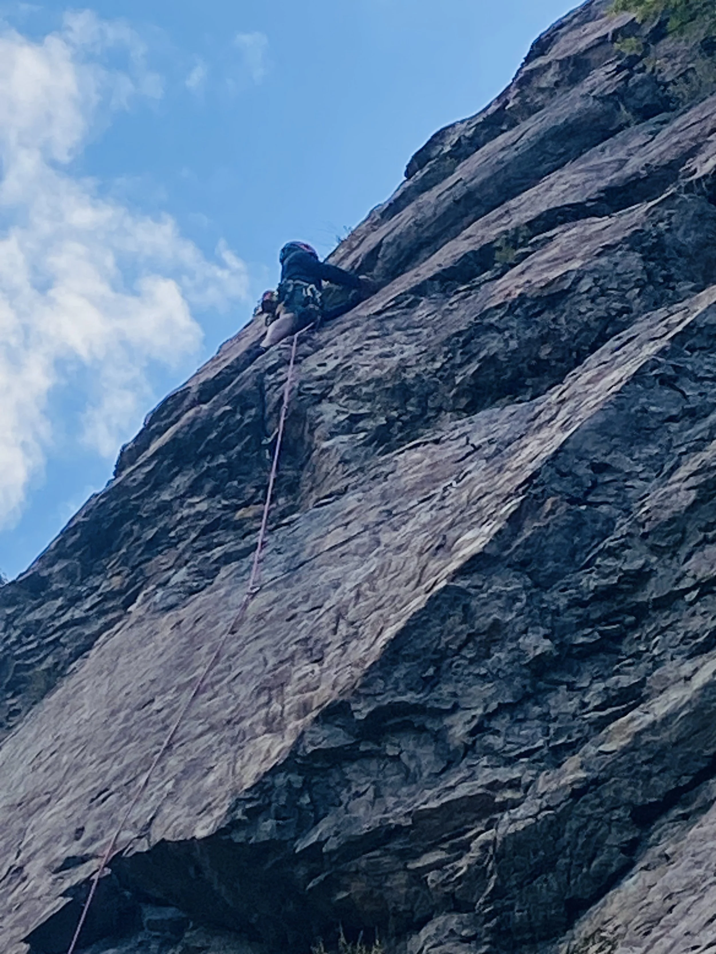 A person climbing a steep rocky cliff with climbing gear and rope.