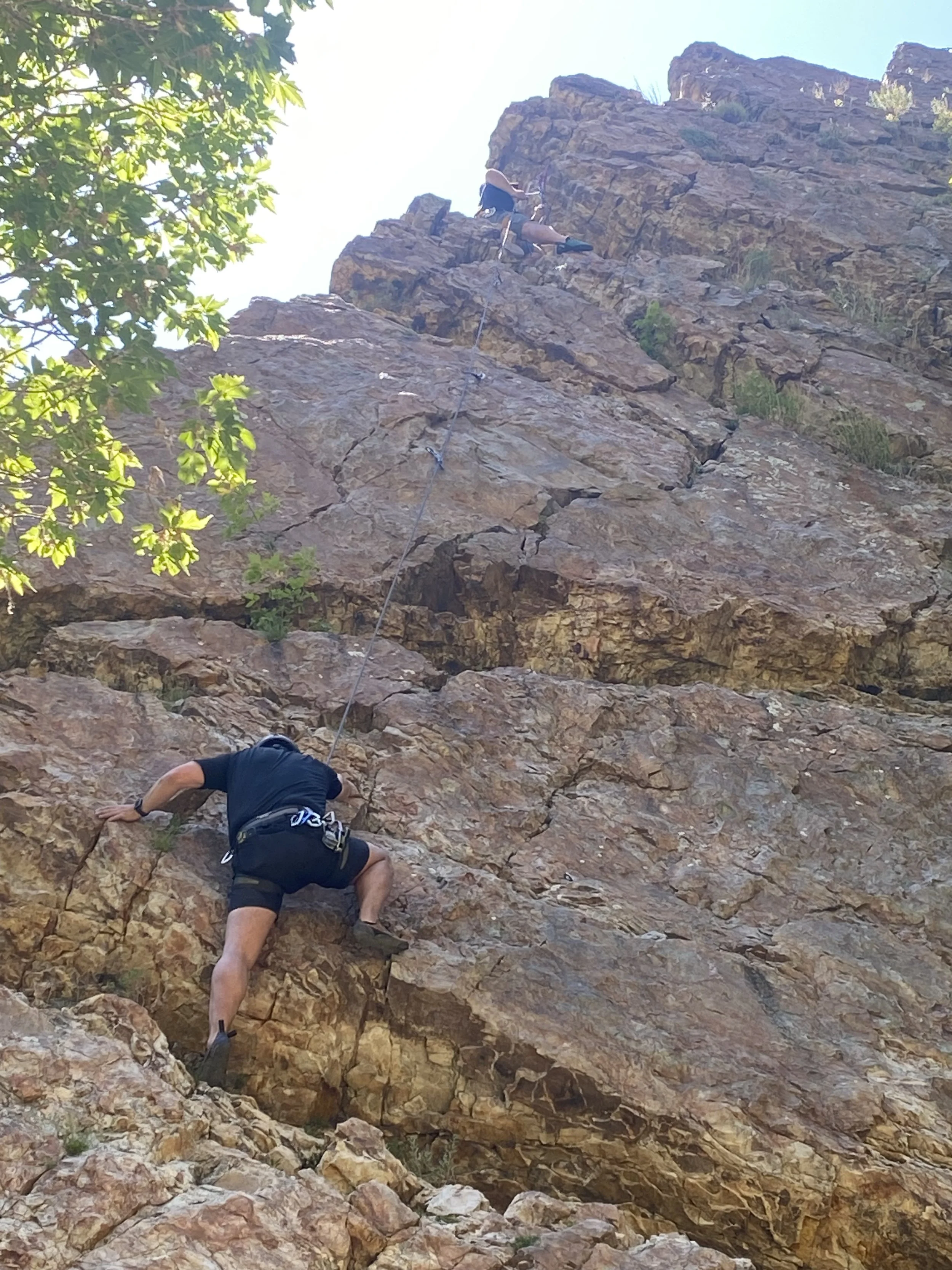 Two people are rock climbing on a steep, rocky cliff. One climber is ascending lower on the rock face, while the other higher up, with a safety rope attached to each of them.