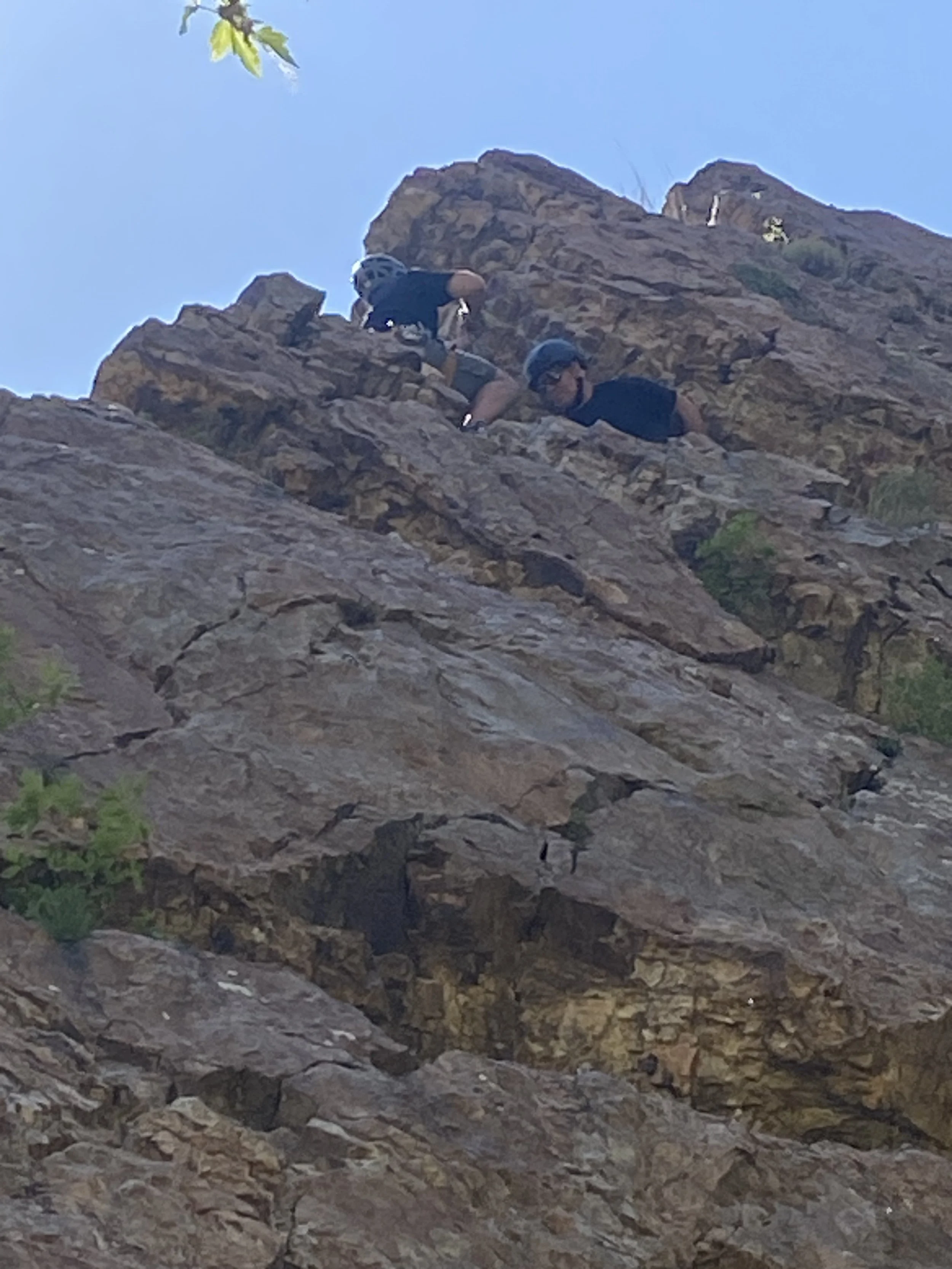 Two people climbing a rocky mountain, both wearing helmets and climbing gear.