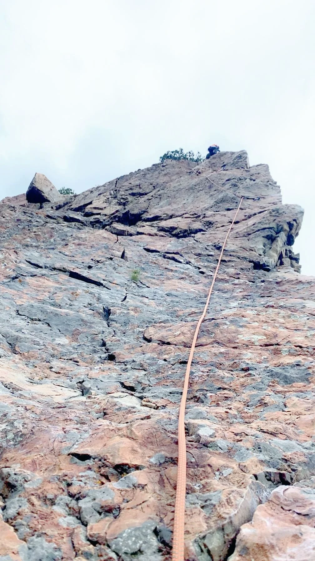 A person climber wearing a helmet and harness ascending a steep rock face with a safety rope attached.