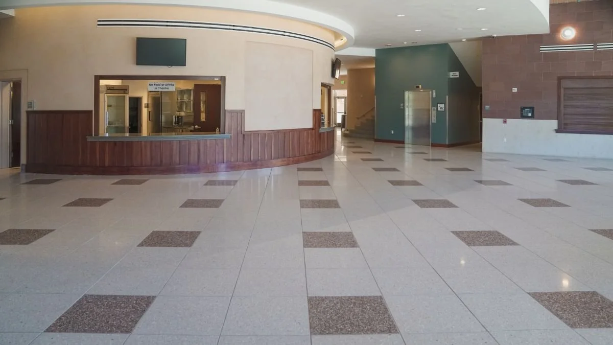 Empty interior lobby with checkered tile floor, reception window, elevator, and stairs.