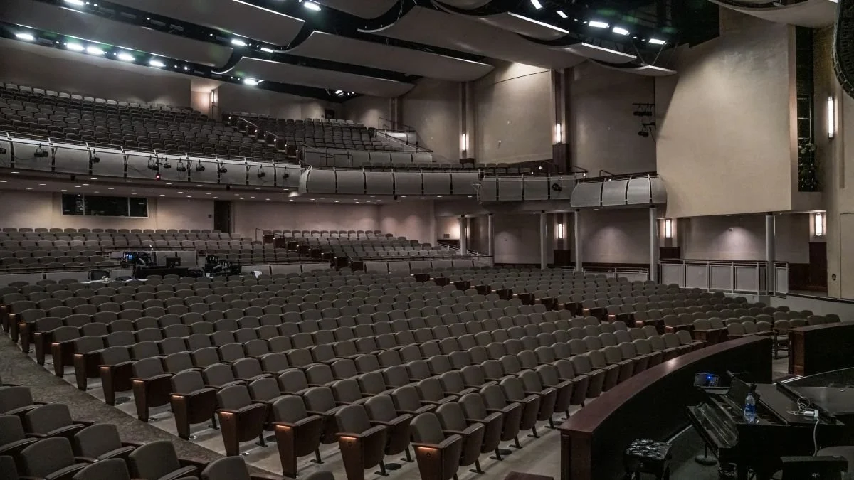 Empty theater with rows of seats, a stage, and a grand piano.