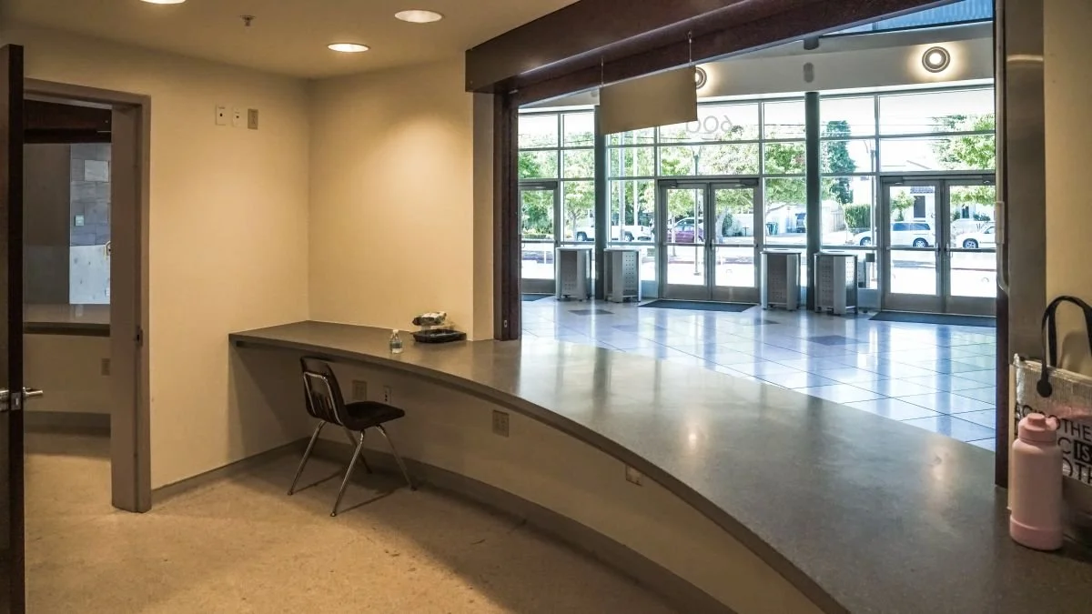 Empty indoor space with a curved countertop, a single chair, and large glass windows showing parked cars outside.