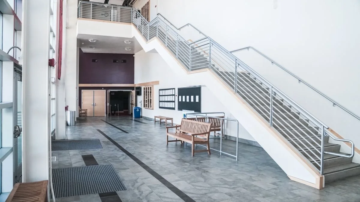 Empty indoor space with a staircase, benches, and a trash can.