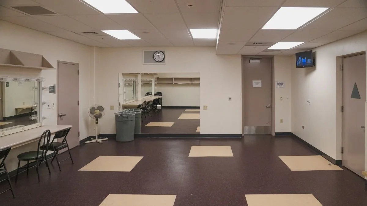 Empty room with chairs, a wall clock, trash cans, small fans, and windowed cubicles, possibly a waiting area or office break room.