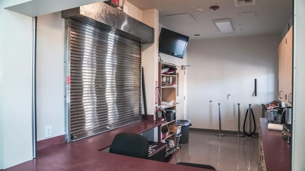 Empty food service area with closed metal shutter, counter, and a small television mounted on the wall.