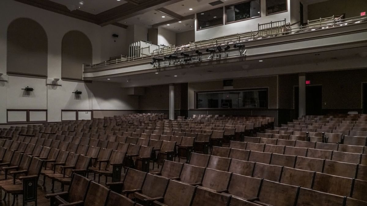 Empty auditorium with rows of wooden seats and balcony with railing