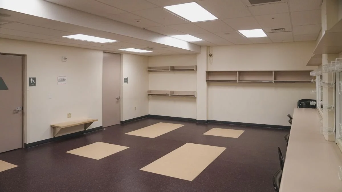 Empty room with white walls, beige doors, some wall-mounted shelves, a small bench, and a counter with chairs.