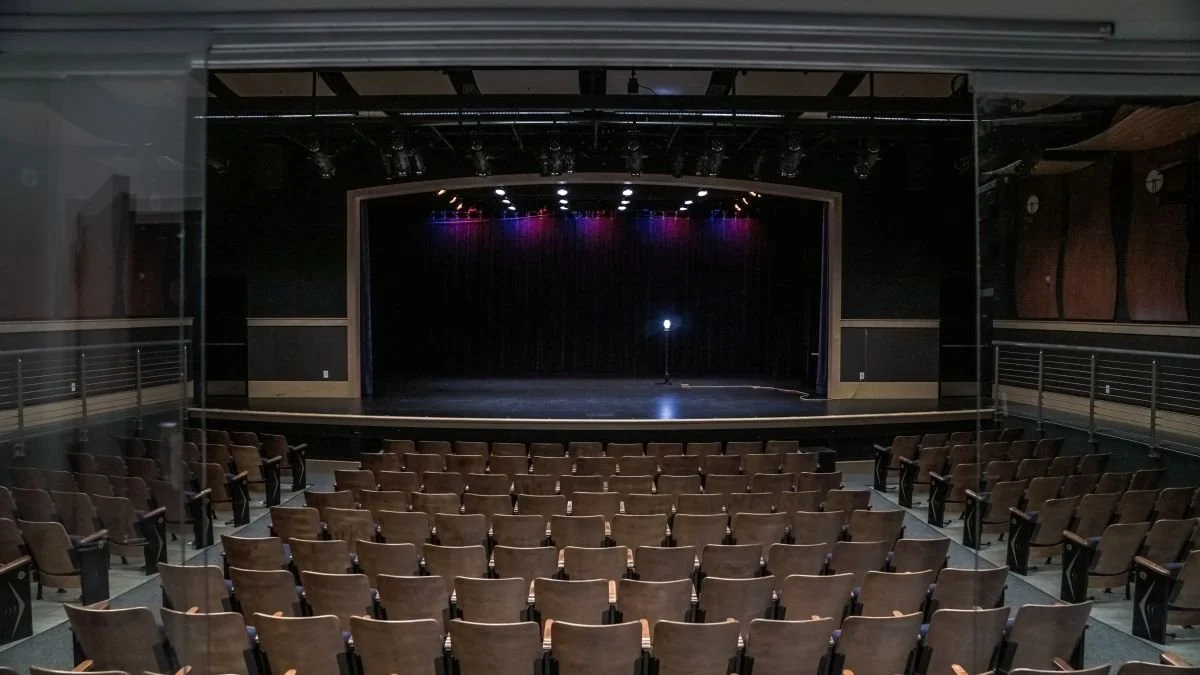 Empty theater with a stage, curtain, and rows of chairs facing the stage
