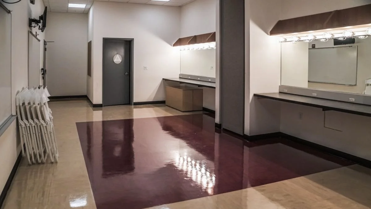 Empty dressing room with mirrors, countertops, folding chairs, and a door.