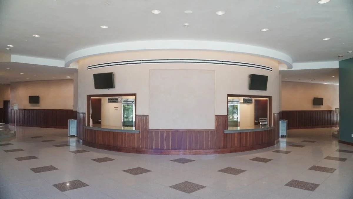 Empty reception area with wooden counters, wall-mounted TVs, and multiple doorways leading to other rooms.