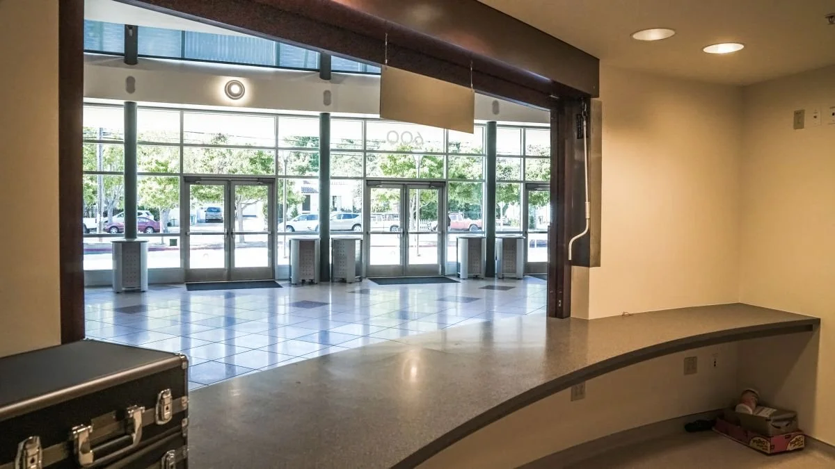 Empty interior space with a curved counter and large glass windows and doors showing a parking lot with cars outside.