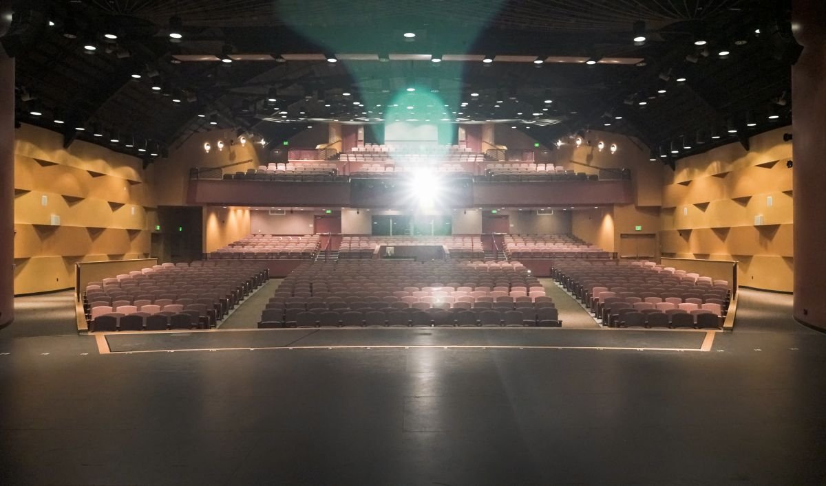 The interior of a theater or auditorium with empty seats, a stage, and a bright spotlight shining from the back.