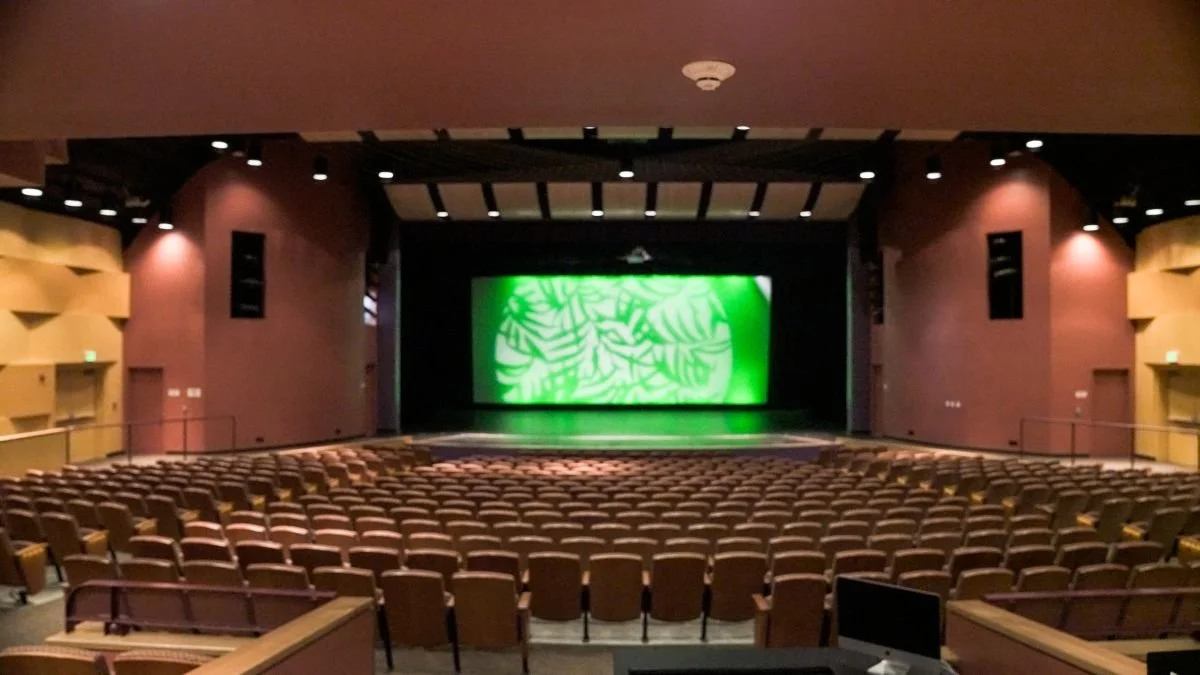Empty auditorium with a stage and a large green digital display at the back of the stage