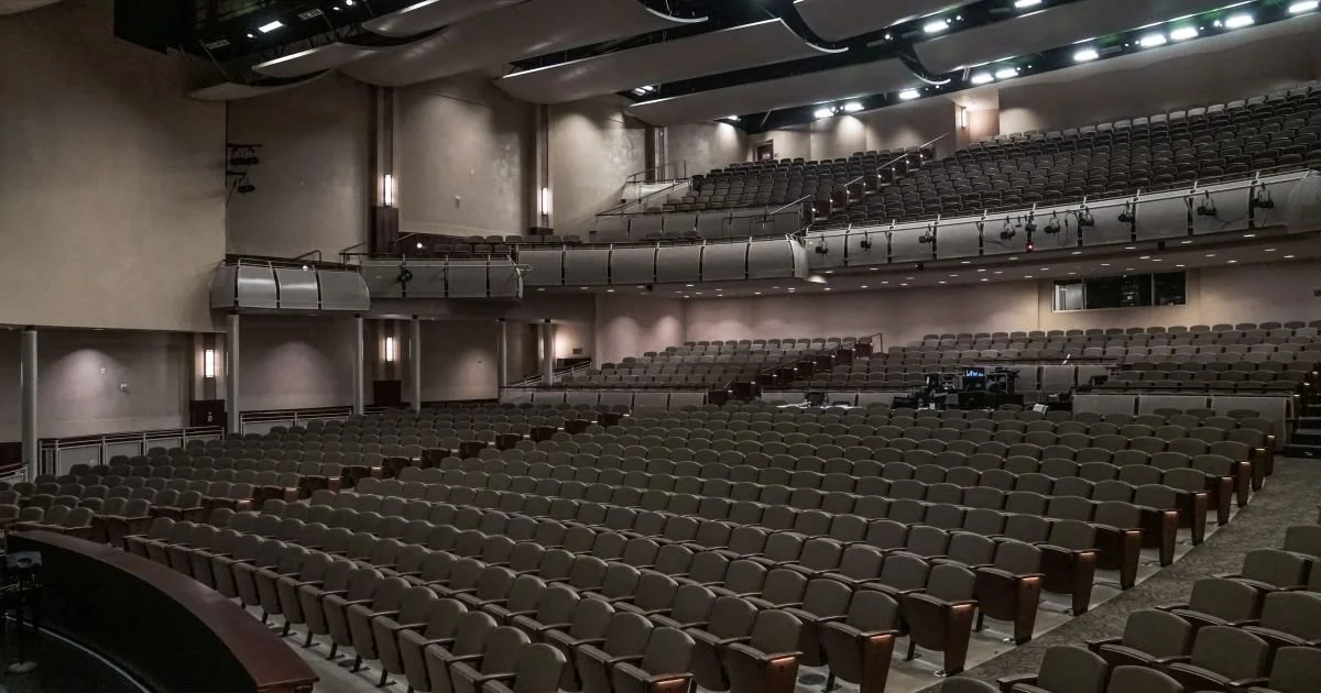 Empty auditorium with rows of chairs and a stage area in the front.
