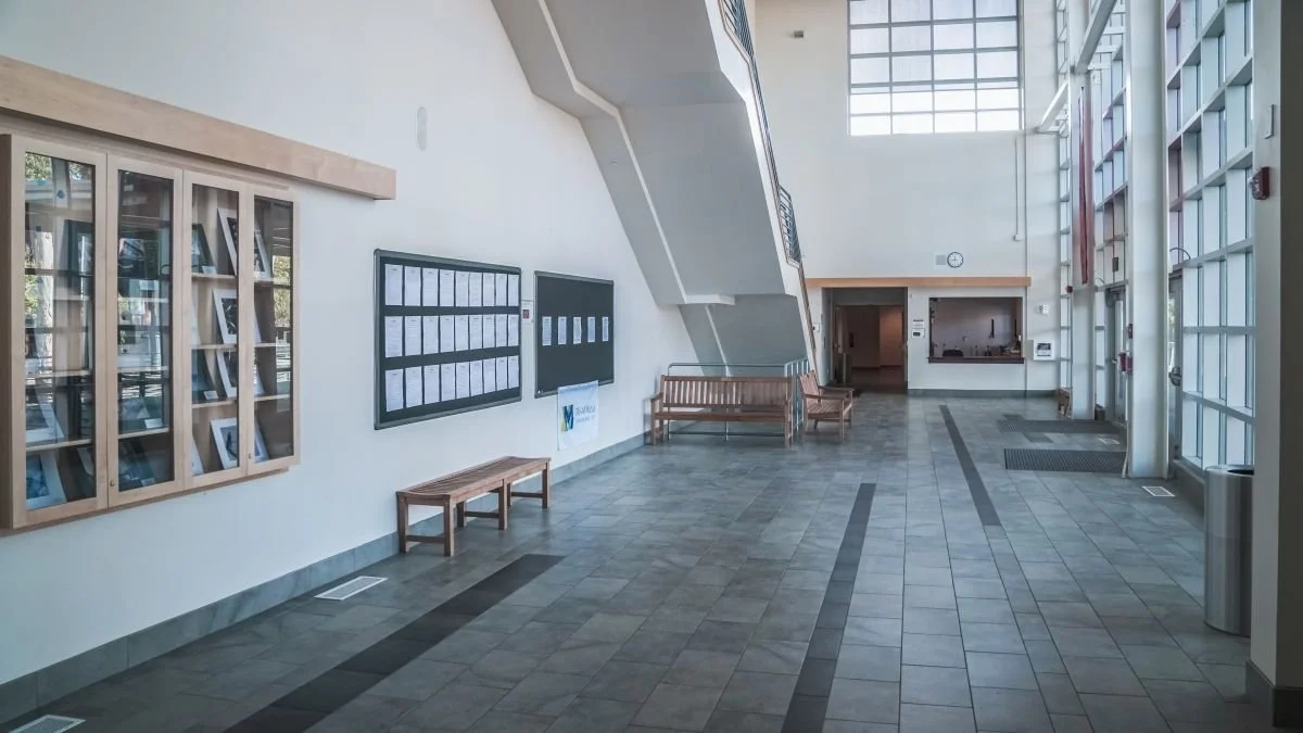 Empty modern lobby area with benches, wall display cases, a large window, and glass doors.
