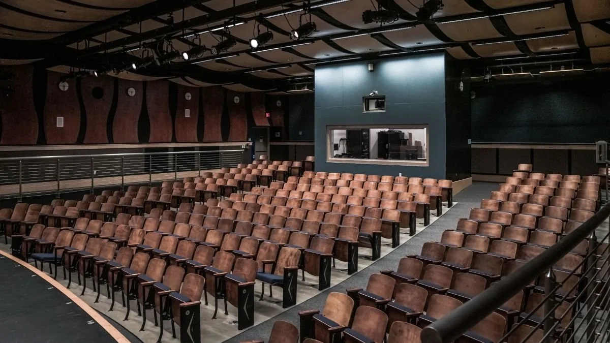 Empty auditorium with brown chairs arranged in rows, a small windowed control room, and a dark, stylish interior design.