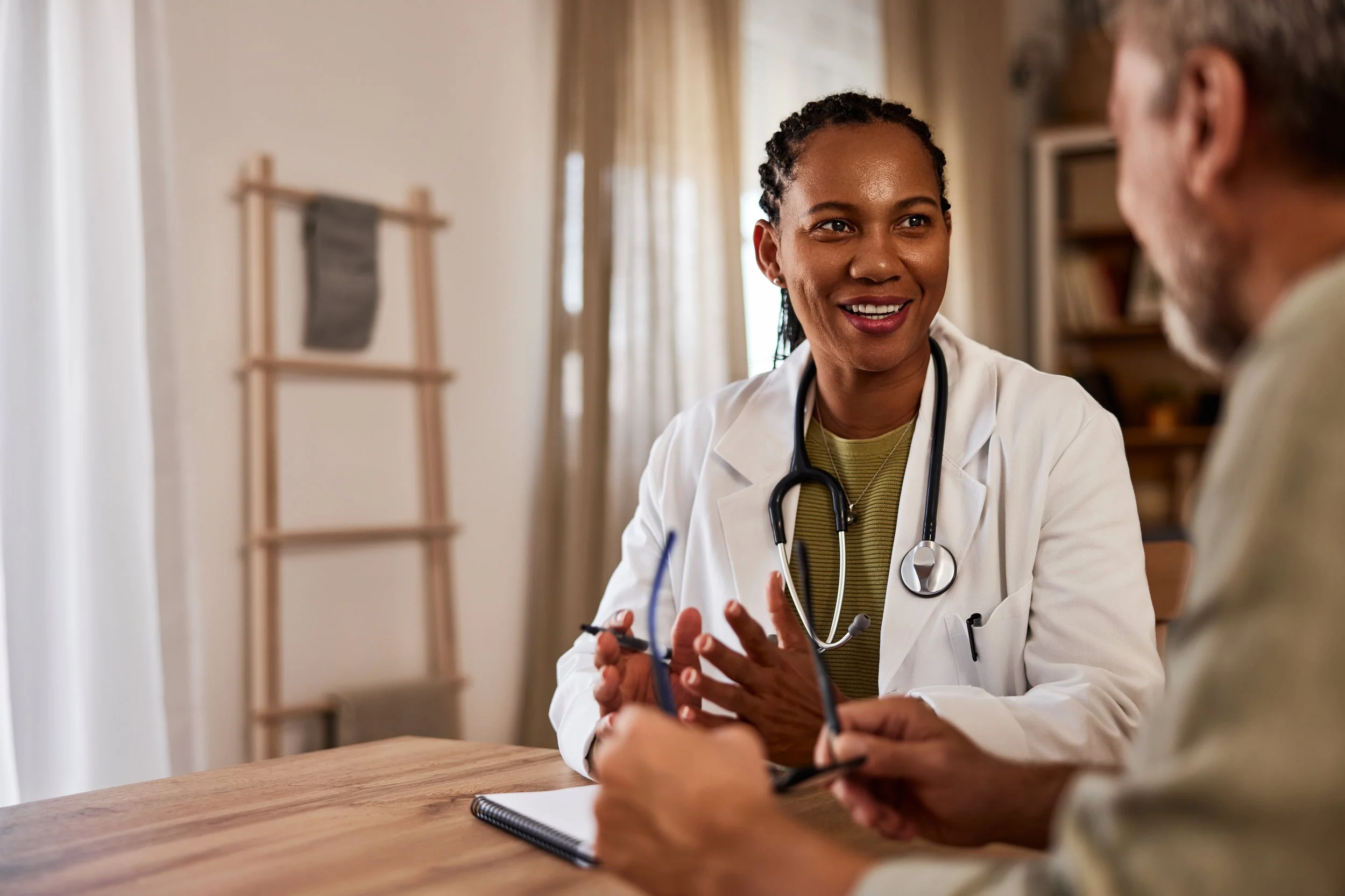 Female doctor talking with an older male patient in a consultation room, both smiling, in a medical setting.