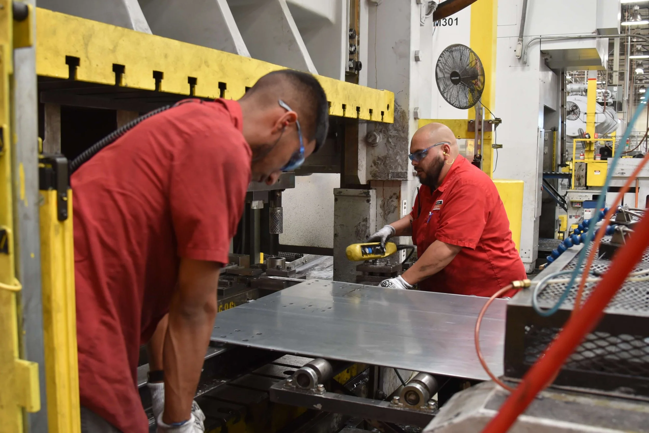 Two workers in red shirts in an industrial manufacturing facility. 