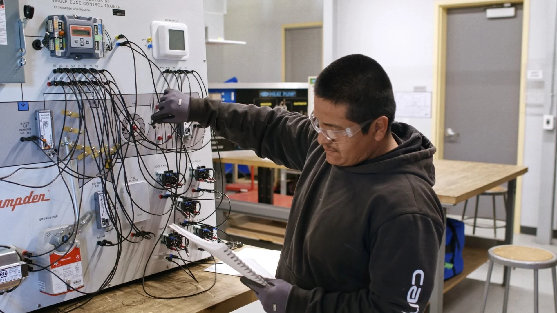 A man wearing safety glasses and gloves working on an electrical control panel