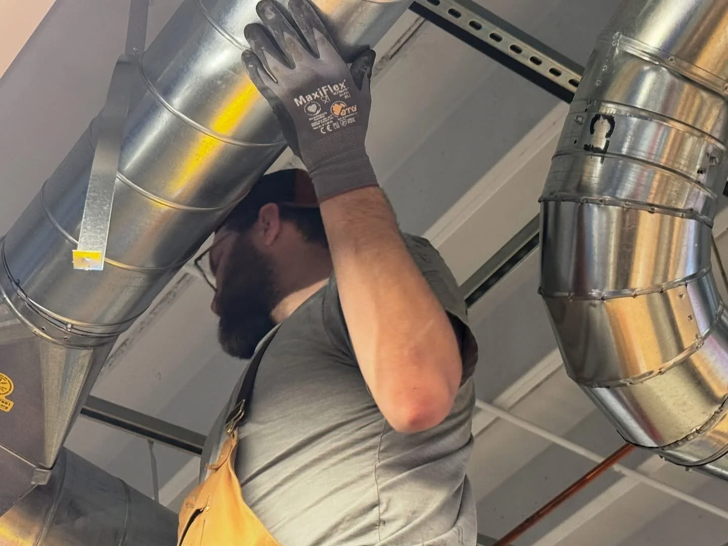 Three technicians working on an electrical or HVAC unit wearing protective gear