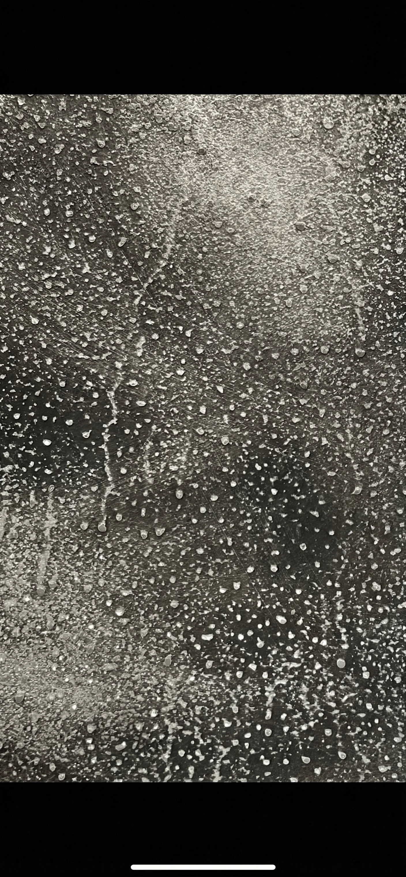 Gocce di acqua su una superficie trasparente, forse vetro, con riflessi di luce.