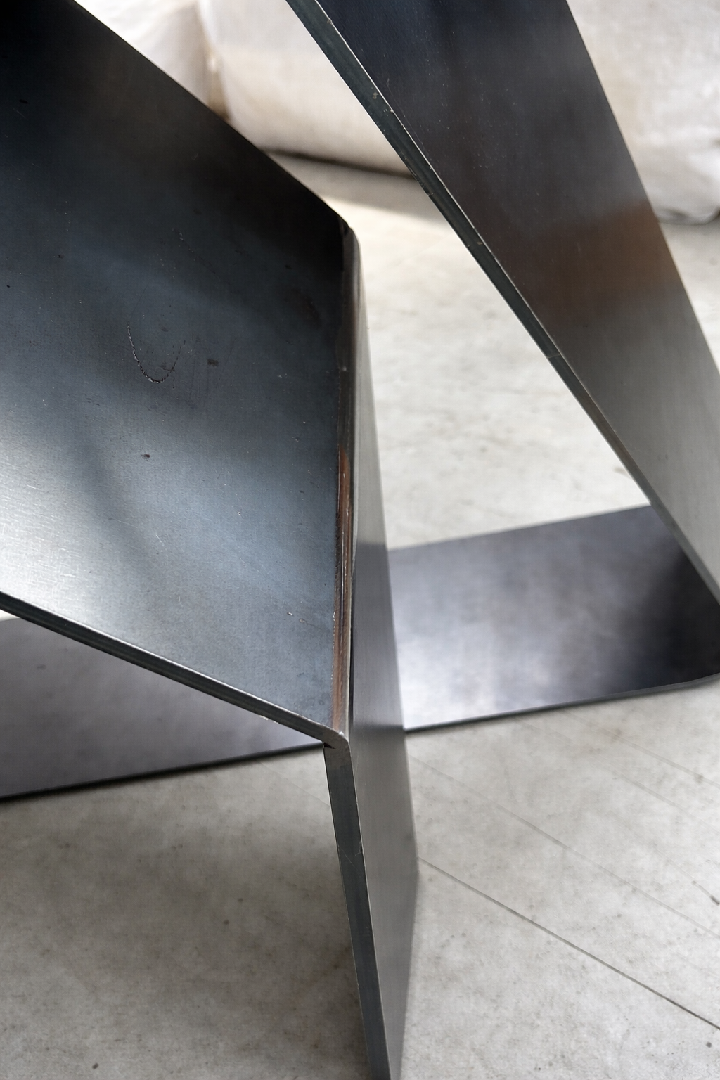 Particolare di una sedia di metallo di colore nero con superfici lisce e angoli vivi, posta su un pavimento chiaro.