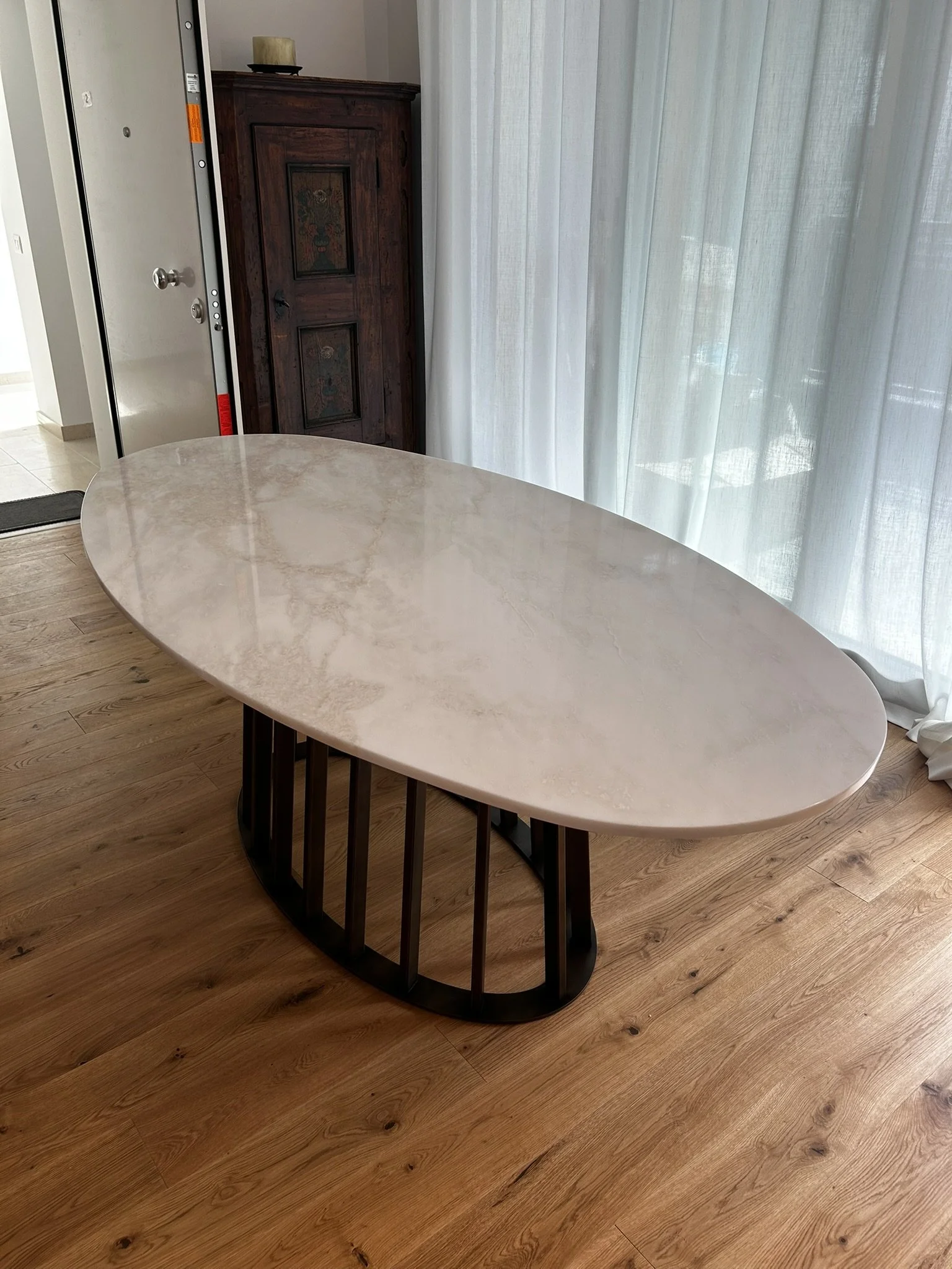 Tavolo da pranzo o da soggiorno con piano in marmo bianco e base in legno scuro, vicino a una finestra con tenda leggera e una credenza in legno scuro