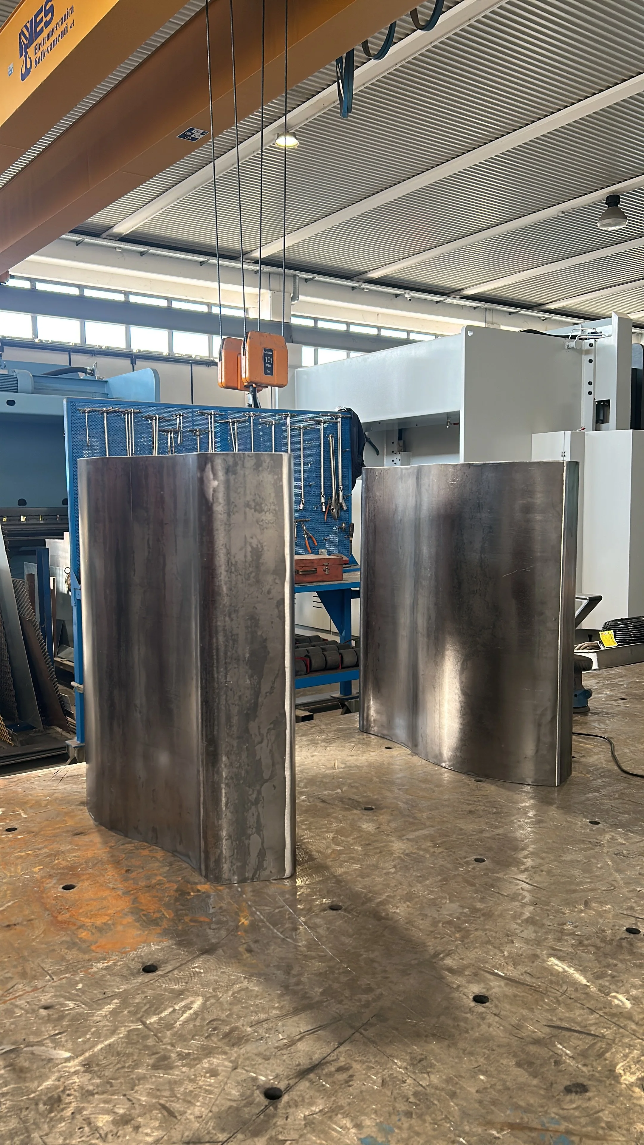 Due grandi pannelli di metallo curvi in un ambiente industriale, con strumenti e attrezzature sullo sfondo.