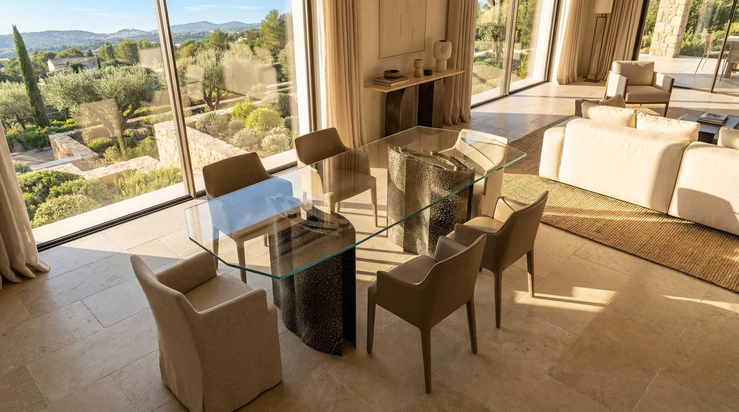 Interno di una stanza con tavolo in vetro e sedie, vista su giardino con alberi e paesaggi collinari attraverso ampie finestre