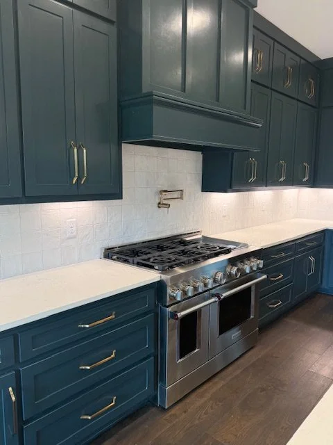 Kitchen with dark teal cabinets, white countertops, white tiled backsplash, and a stainless steel stove with oven.