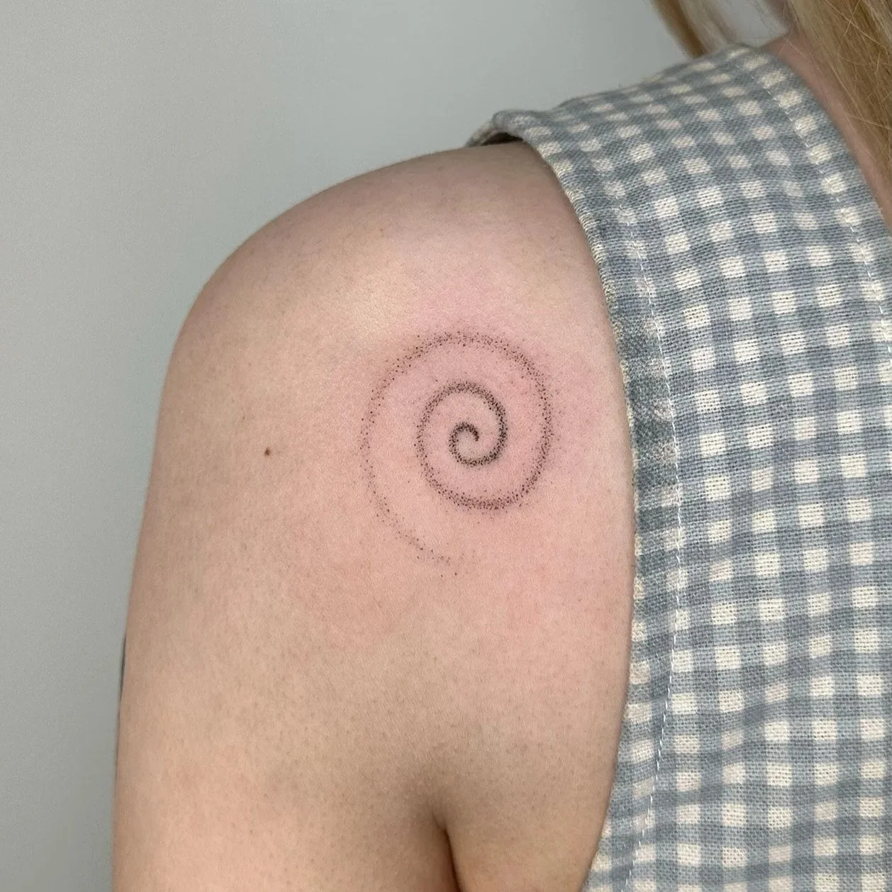 A person's upper arm with a spiral-shaped tattoo drawn with small dots.