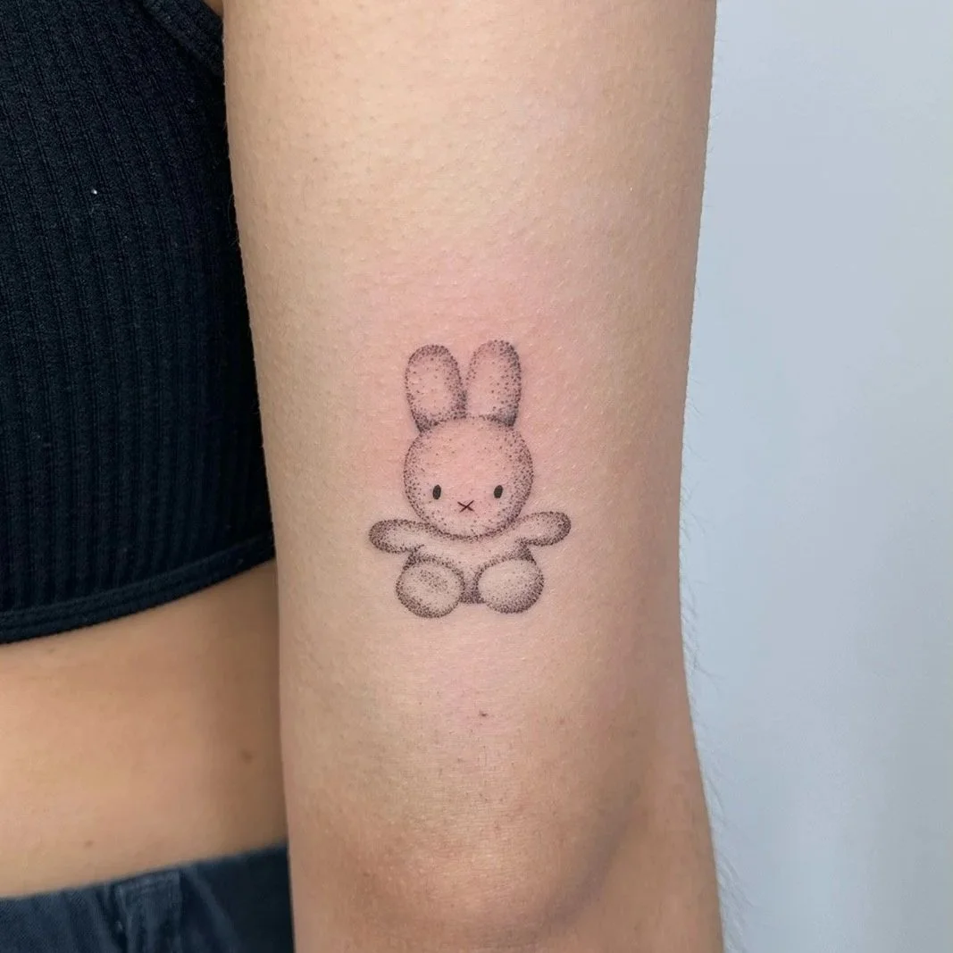 Tattoo of a cute, minimalist bunny sitting with its front paws raised.