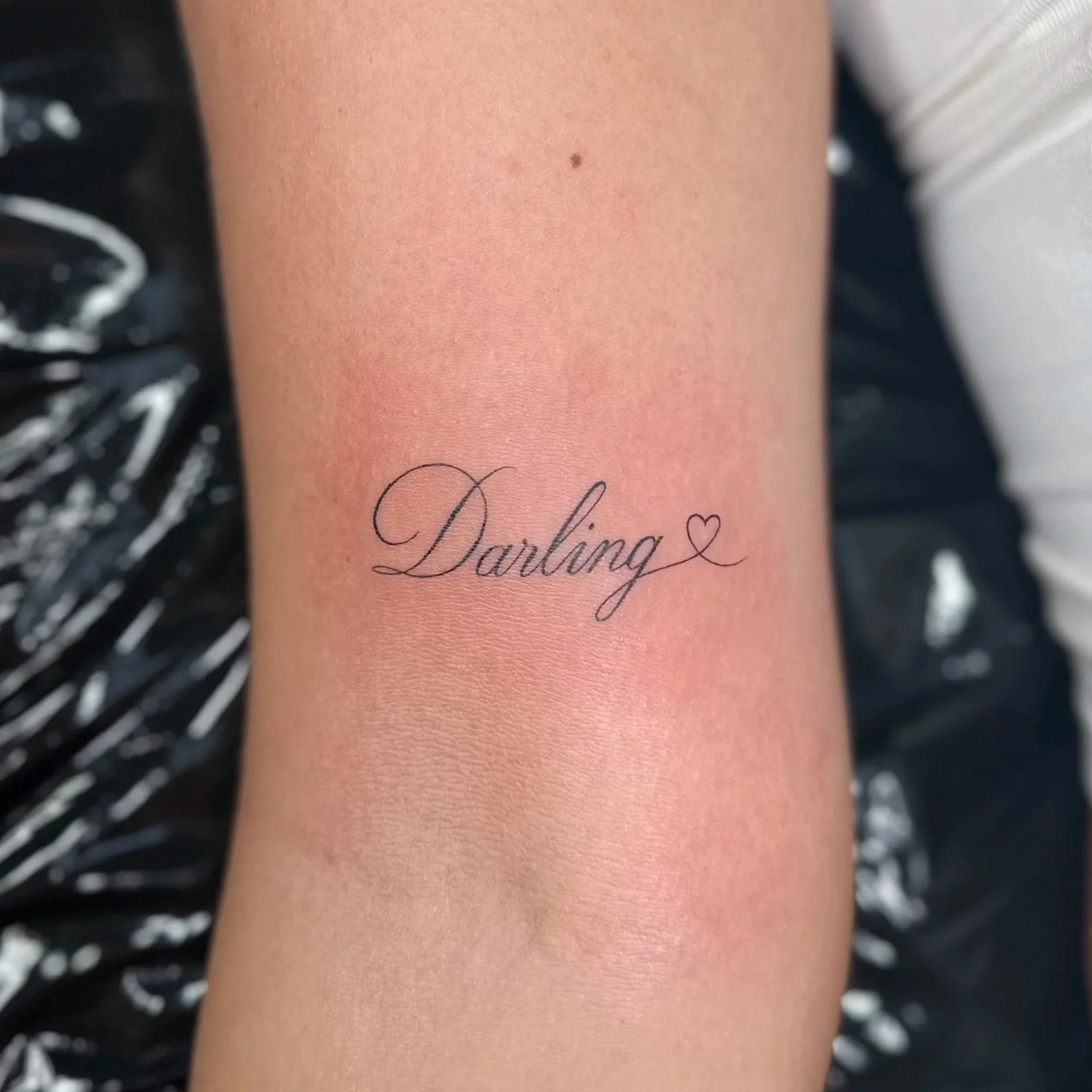 A person's side torso with a floral tattoo, featuring two lilies with flowing stems and petals, in delicate black ink.