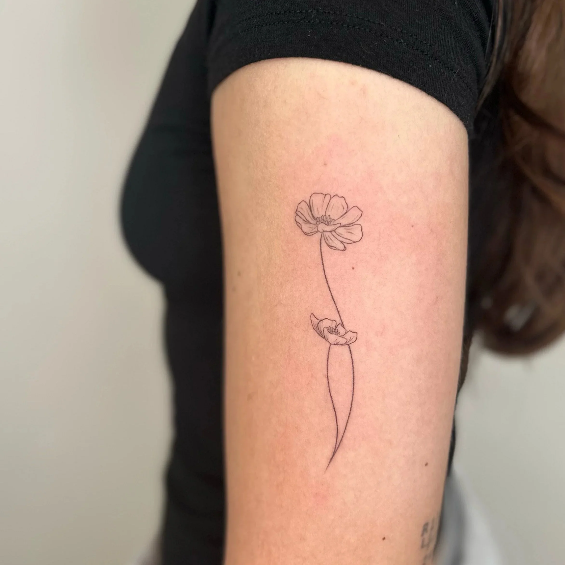 Line art tattoo of two flowers on a person's upper arm.