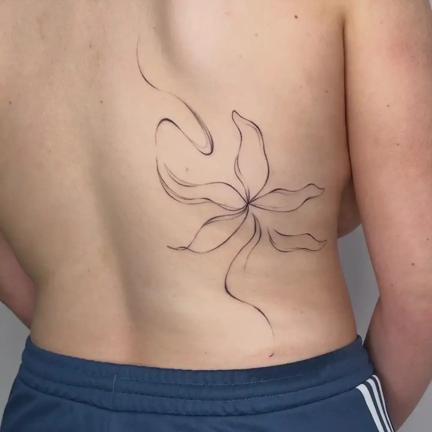 A person's side torso with a black line art tattoo of a flowing flower on the skin.
