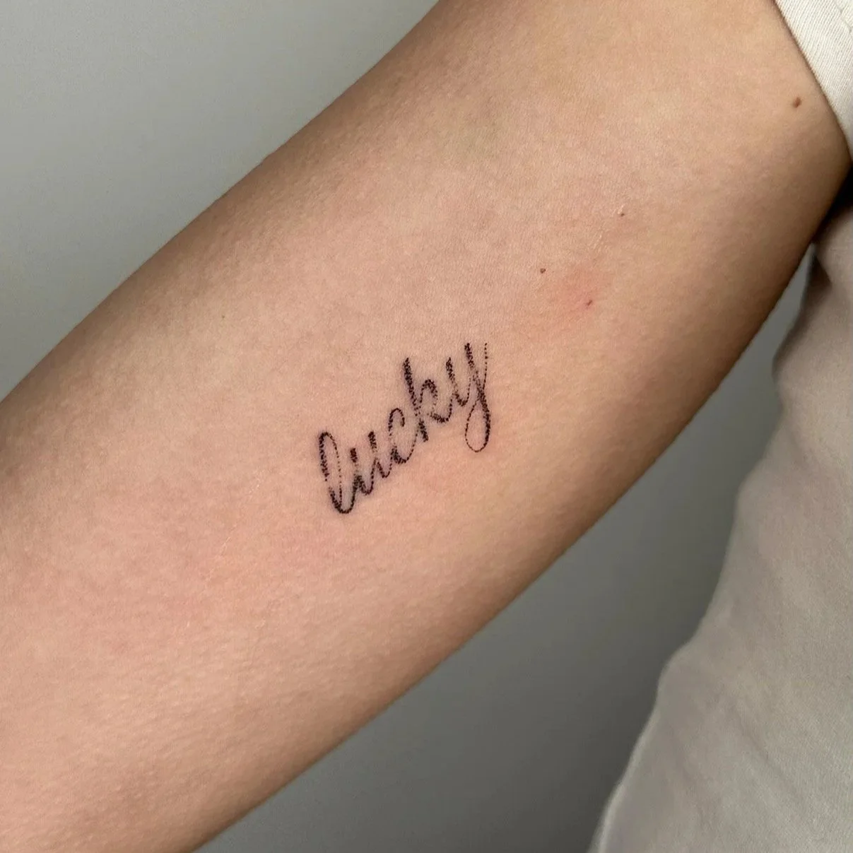 Close-up of a person's inner forearm with a tattoo that says 'lucky' in cursive ink.