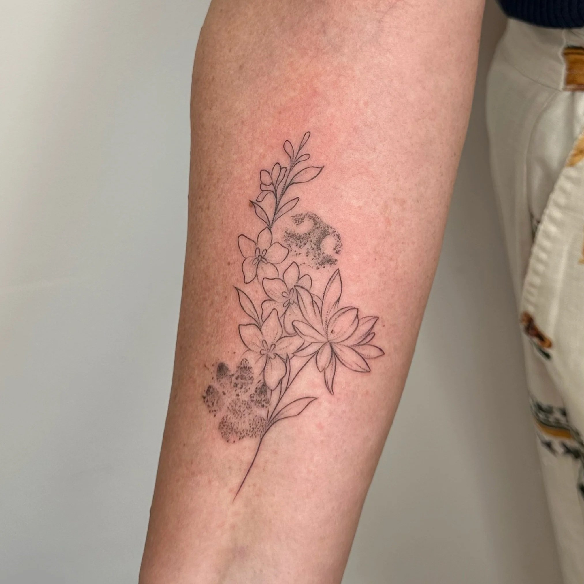 A tattoo of outlined flowers and leaves on a person's arm, with some shaded areas resembling a fingerprint pattern.