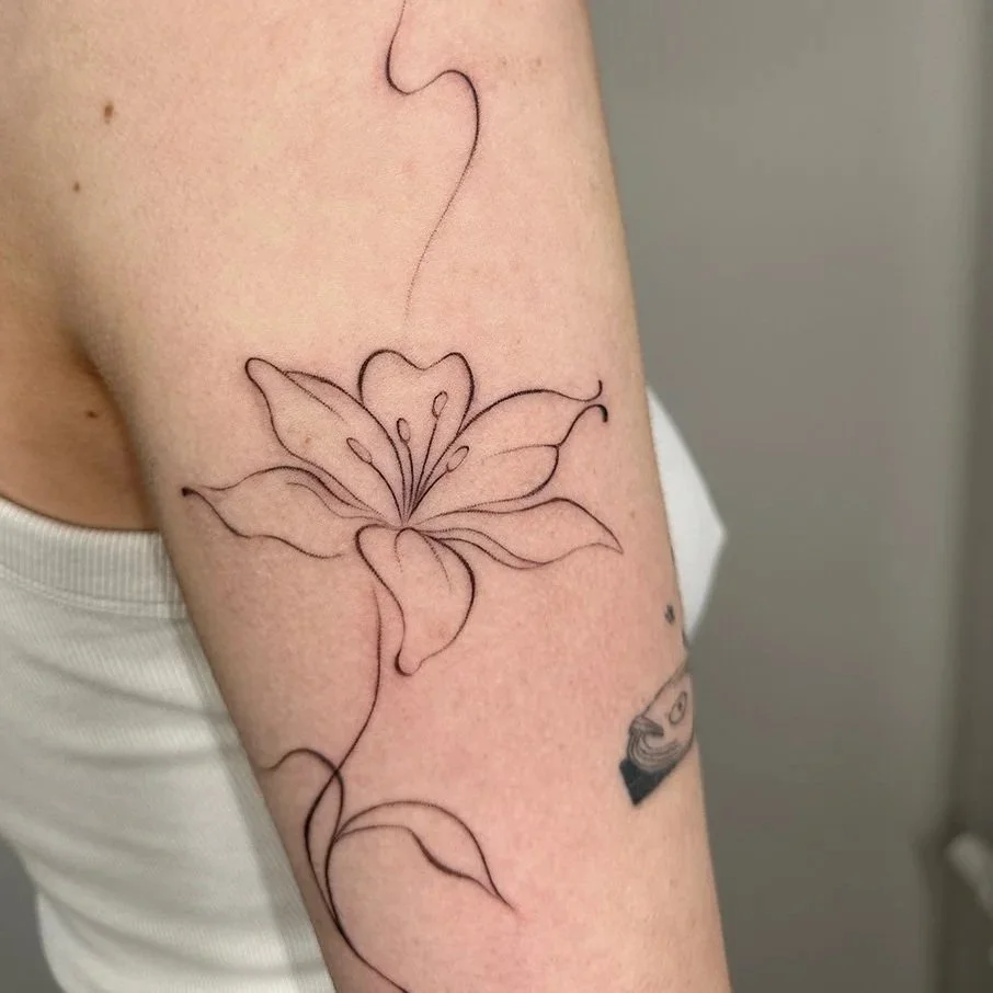 Line art tattoo of a lily flower on a person's upper arm.