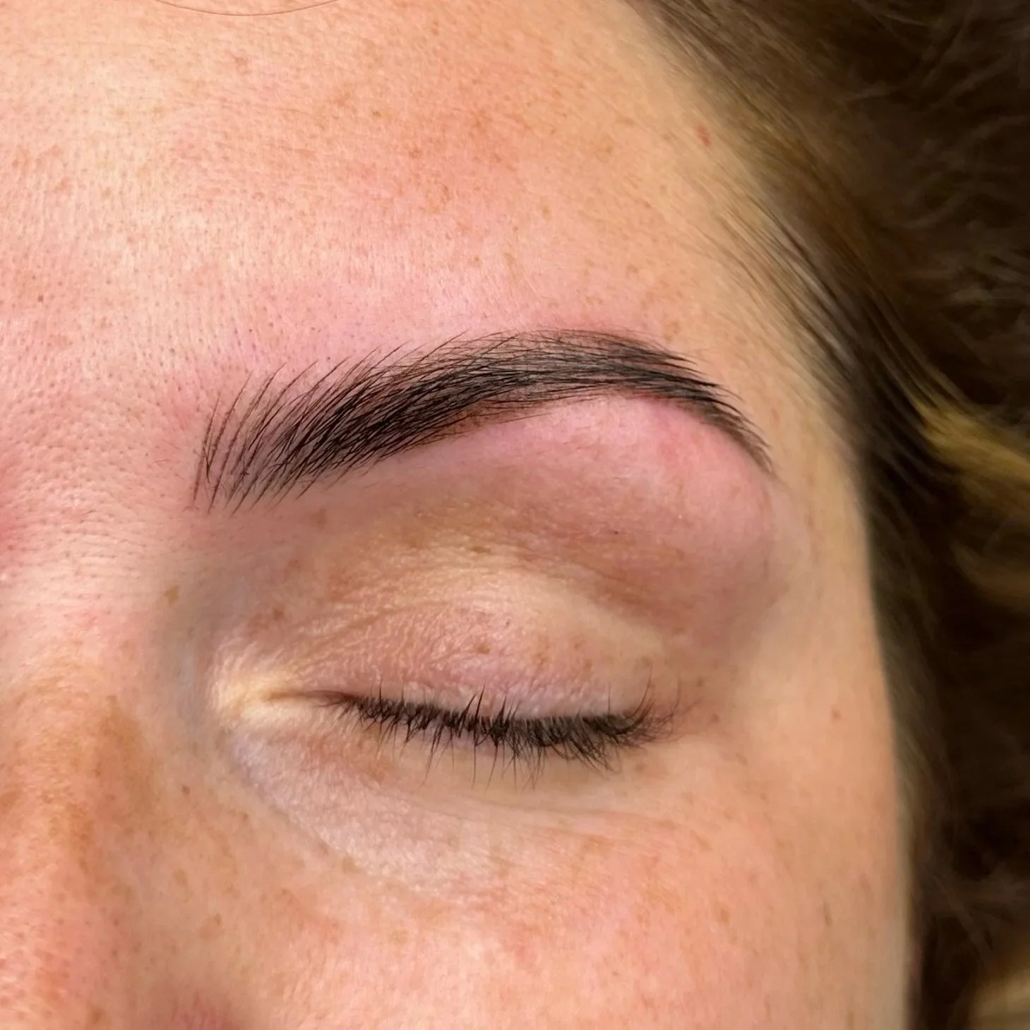 Close-up of a woman's eyebrow, closed eye, and part of her forehead, showing smooth skin and natural makeup.