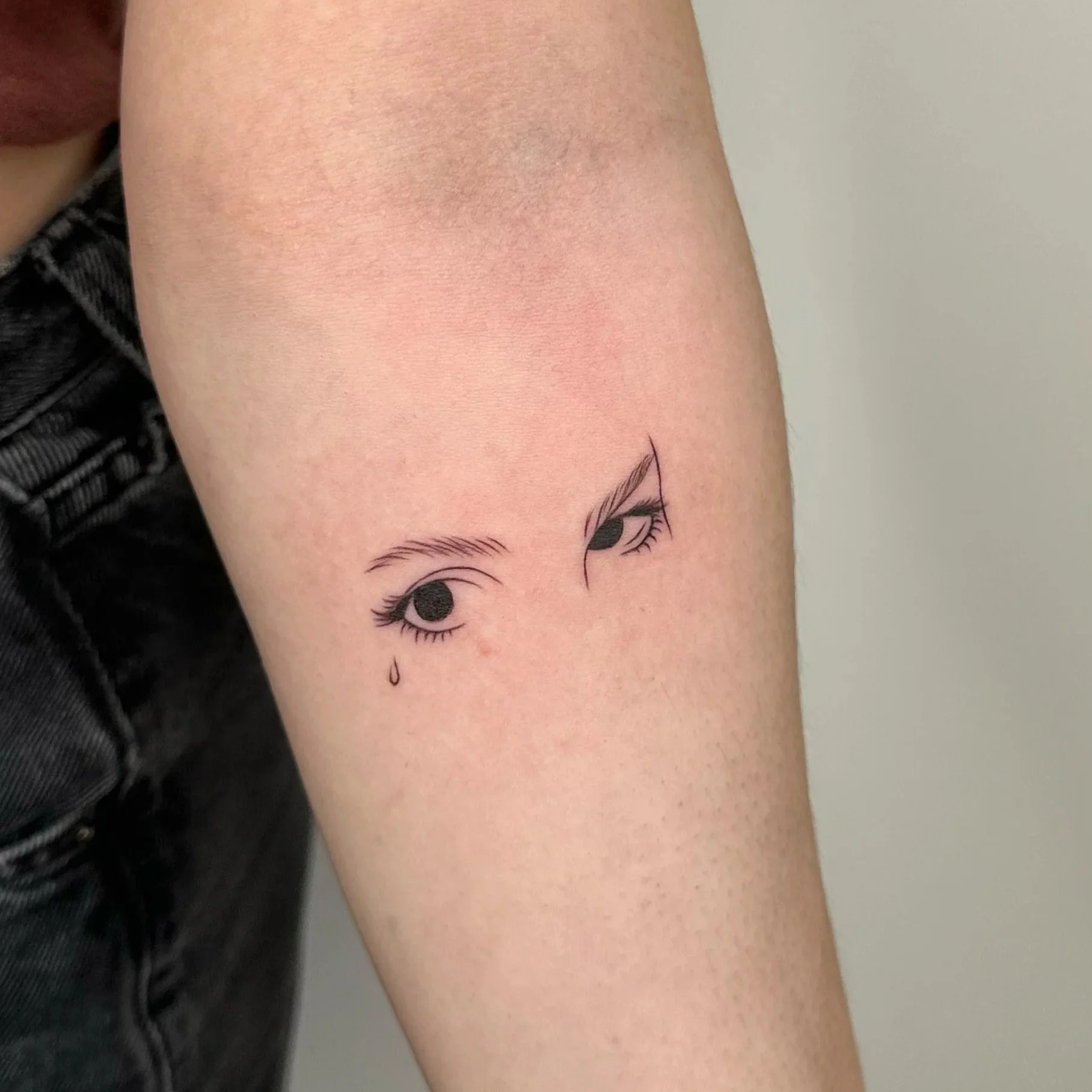 Tattoo of two crying eyes with a tear drop on a person's arm