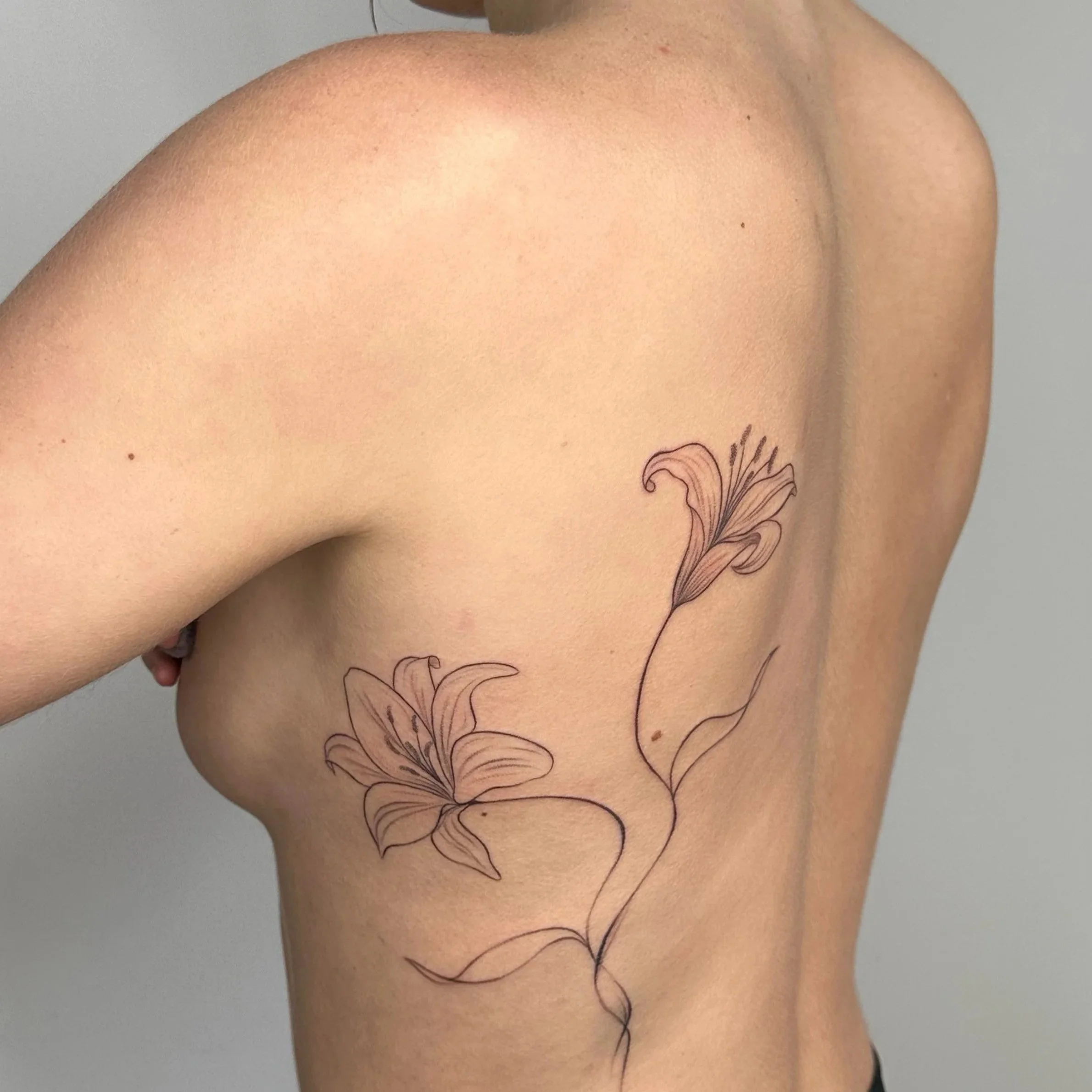 A person's upper torso with a tattoo of two lilies on the side of the chest and rib area.