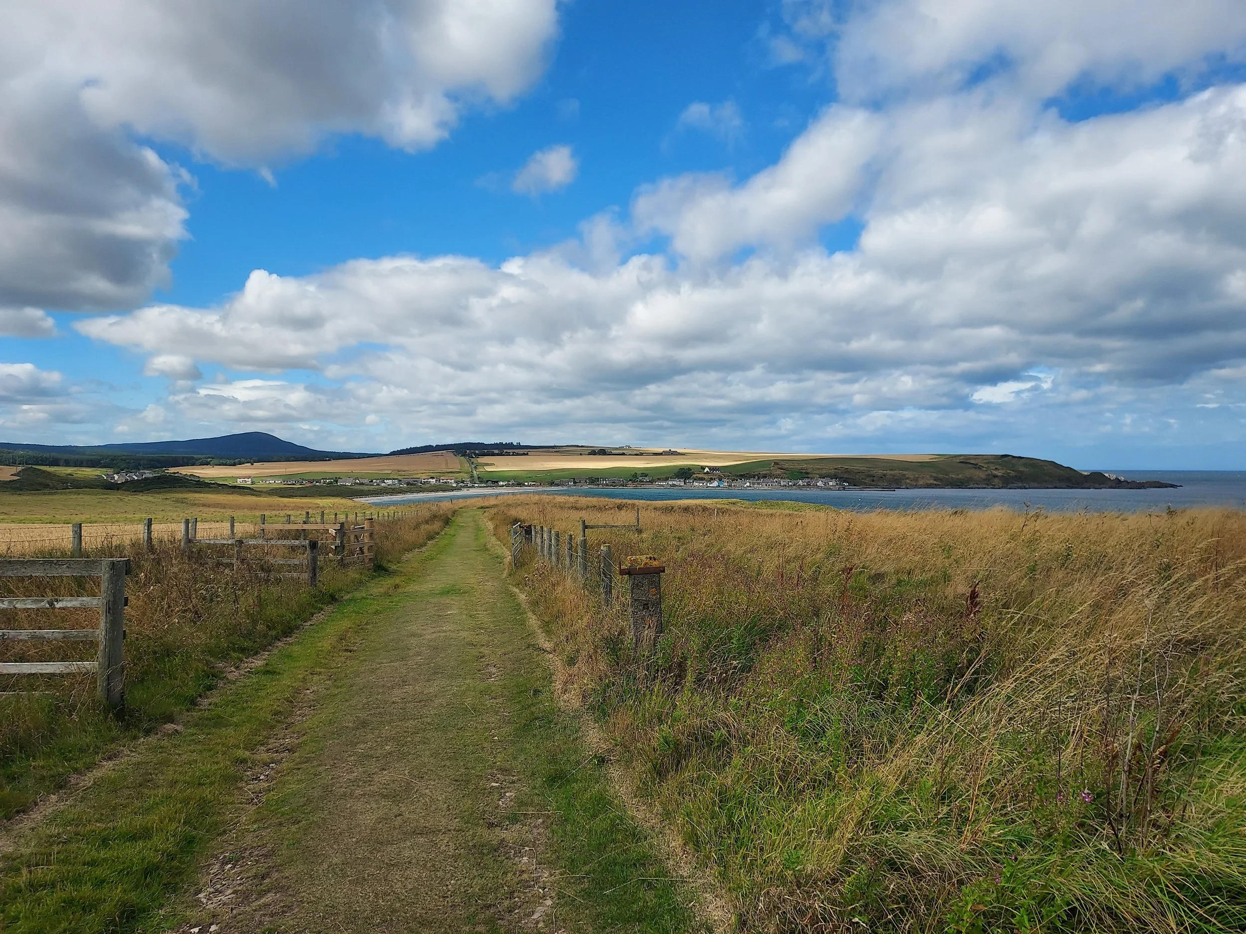 Photo shows a path through fields, towards the distance and the sea